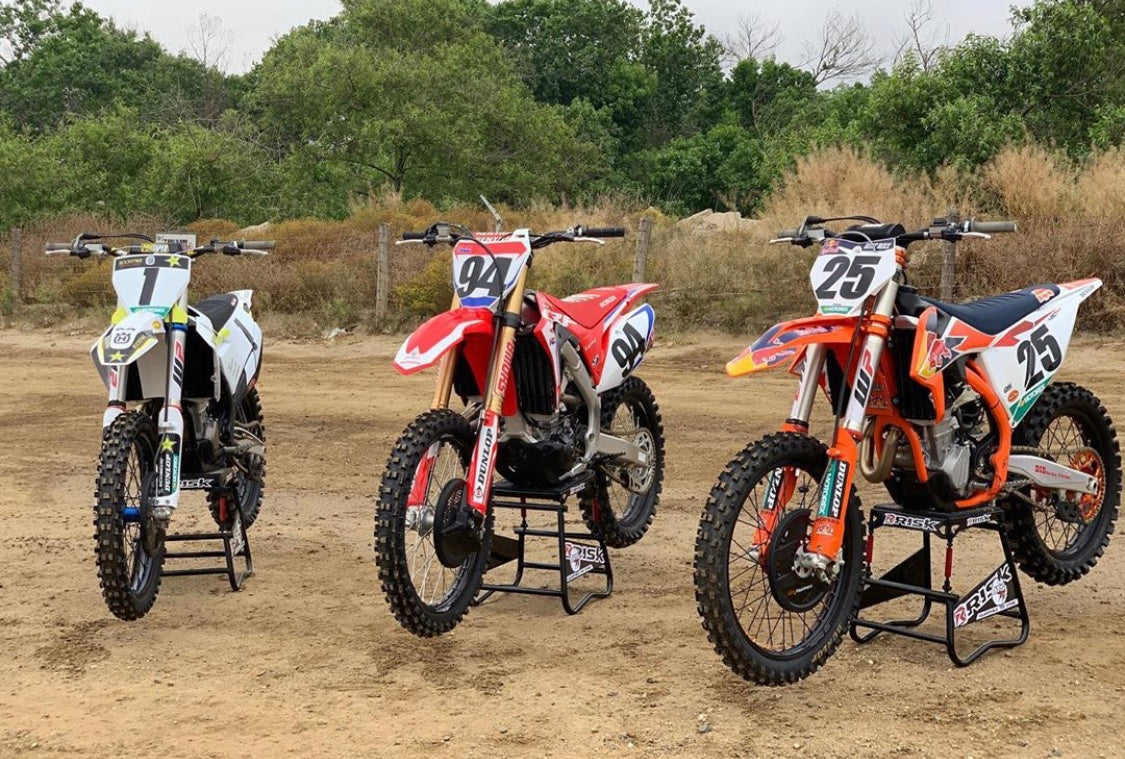Husqvarna, honda, and ktm dirt bikes lined up on risk racing A.T.S. Stands